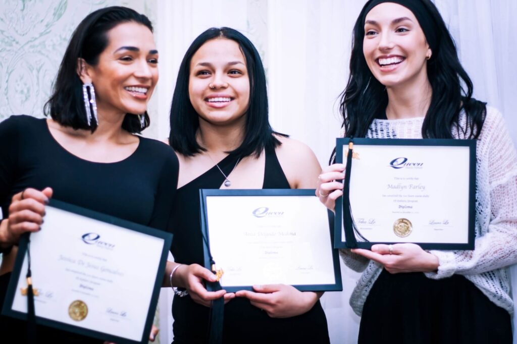 Three QBI cosmetology students holding diplomas at graduation